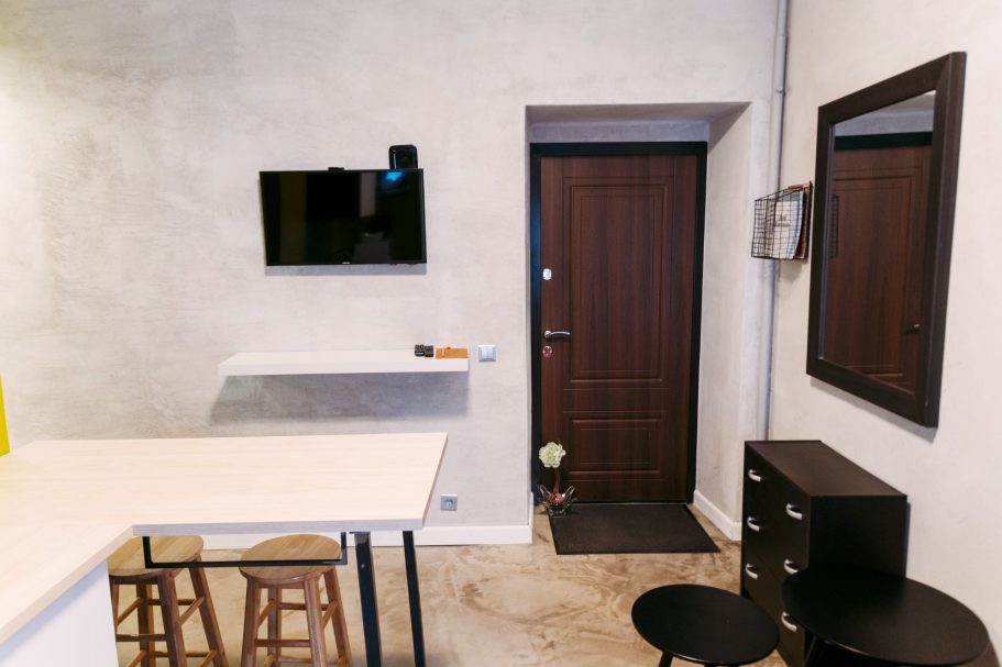 A minimalistic room featuring a door, mirror, TV, and simple furnishings.