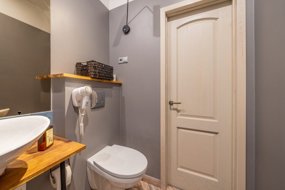 Modern bathroom with a toilet, sink, wooden shelf, and gray walls.
