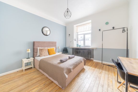 Cozy bedroom with a beige bedspread, blue walls, wooden floor, and a workspace.