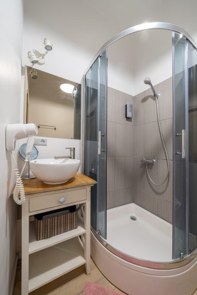Modern bathroom with a curved shower, sink, and wooden storage unit.