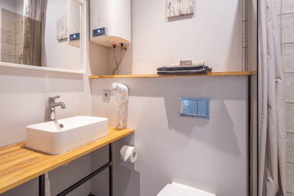 Modern bathroom with a wooden shelf, sink, and shower, featuring minimalistic design elements.