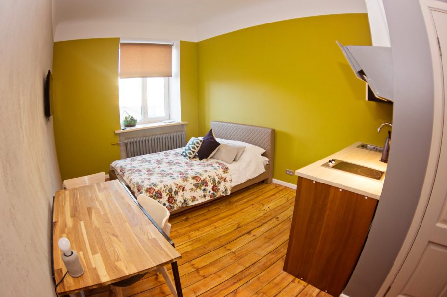 Cozy bedroom with a bed, desk, and a green accent wall. Sunlight from a window.