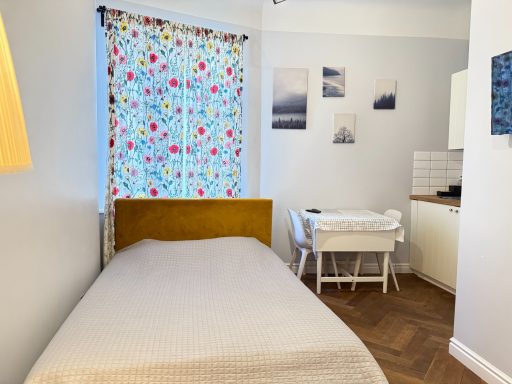 Cozy bedroom with a colorful floral curtain, a bed, and minimalistic decor.