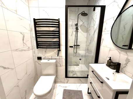Modern bathroom featuring a shower, toilet, sleek vanity, and marble walls.