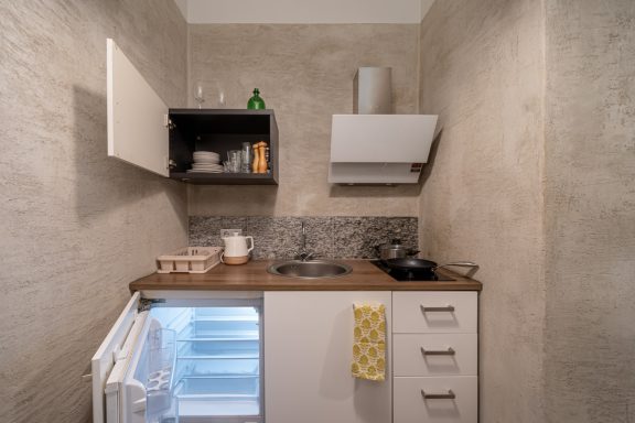 Compact kitchen with a small fridge, sink, and minimal storage, featuring a gray color scheme.