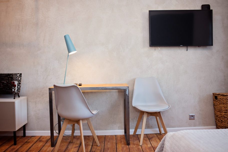 Modern hotel room featuring a desk, two chairs, a lamp, and a wall-mounted TV.