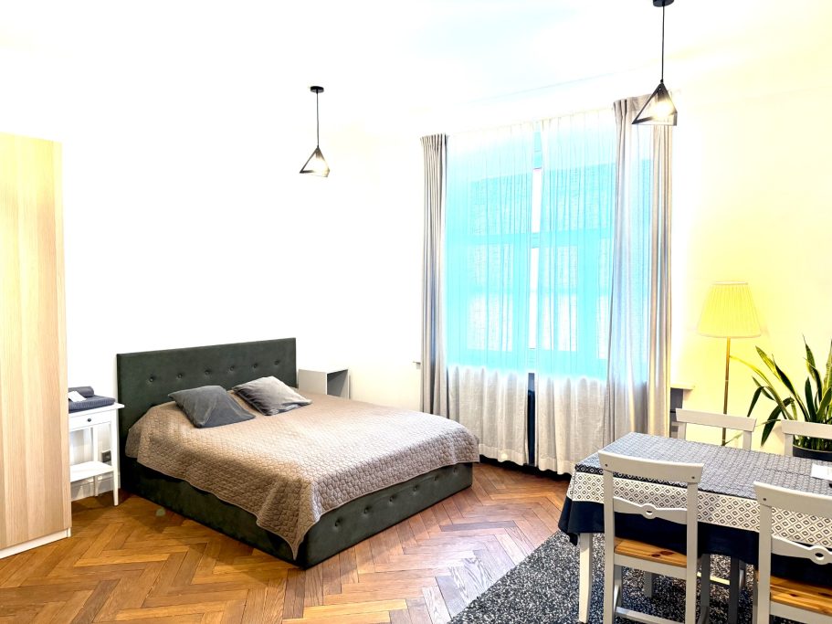 Cozy bedroom with a bed, dining table, and large windows, featuring bright natural light.