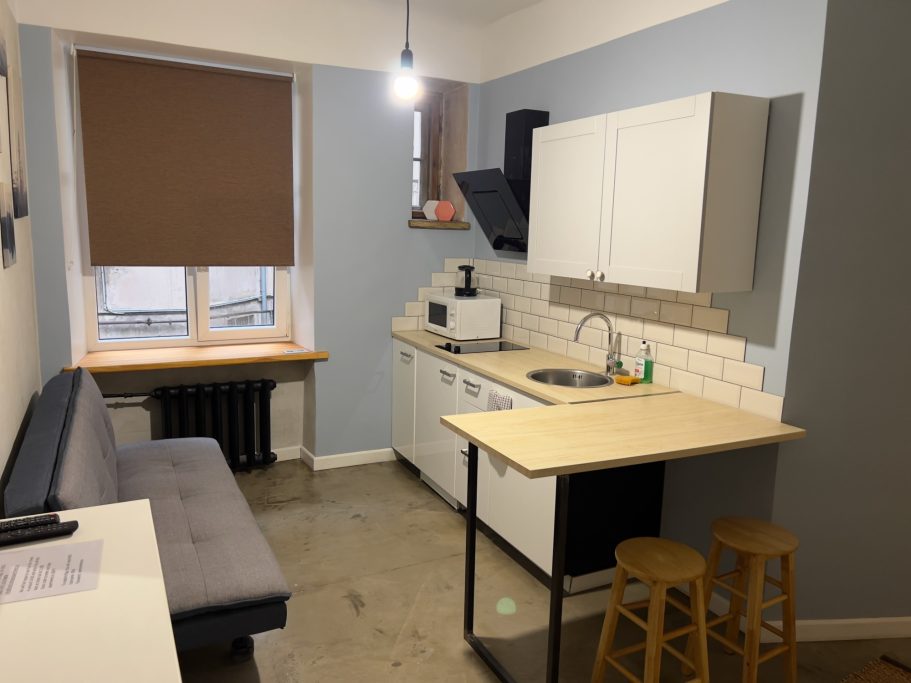Compact kitchen with a sofa, table, and modern appliances against light blue walls.