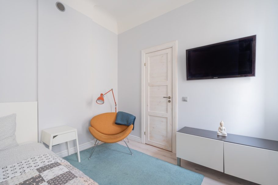 A cozy bedroom featuring a modern orange chair, TV, and minimalist décor.