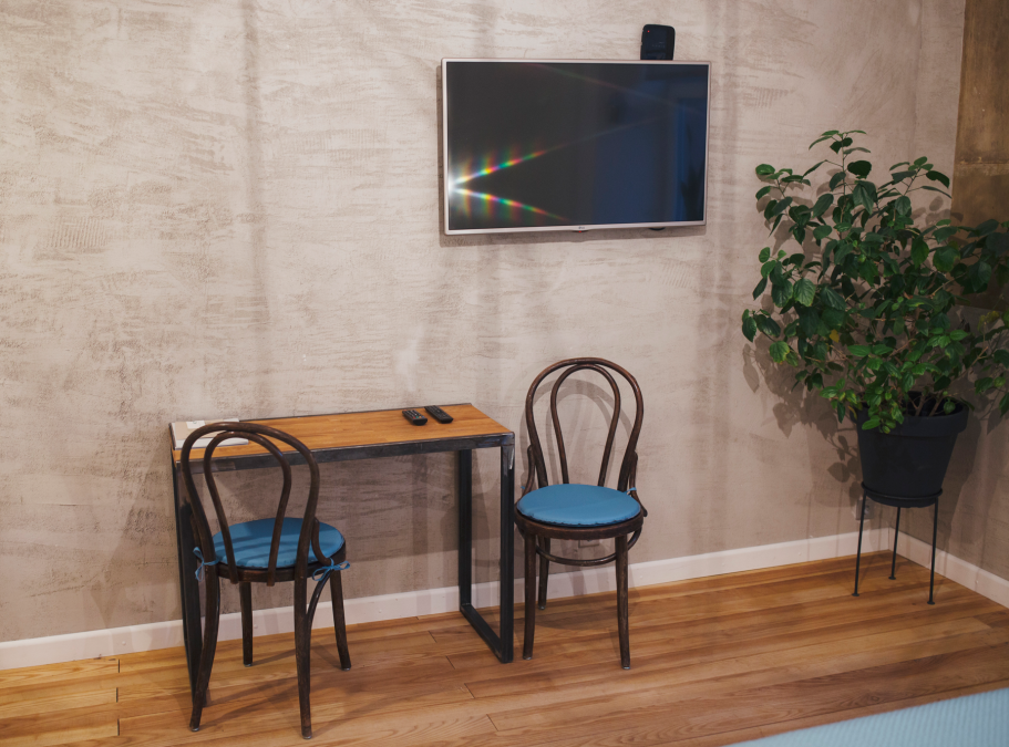 A small table with two chairs, a TV on the wall, and a potted plant nearby.