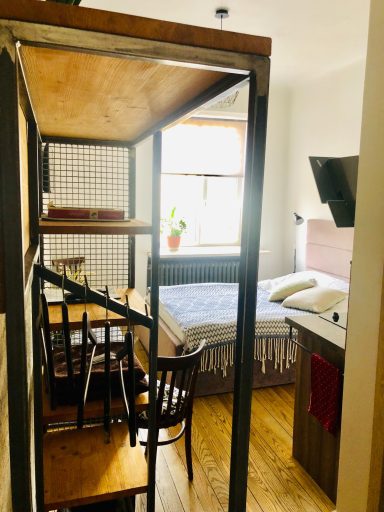 Cozy studio apartment with a bed, dining table, and kitchenette. Natural light from a window.