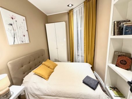 Cozy bedroom with a bed, yellow curtains, and a white bookshelf with books.