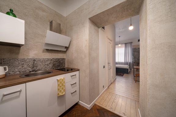 Narrow kitchen corridor with gray walls, wood accents, and a view into a living area.