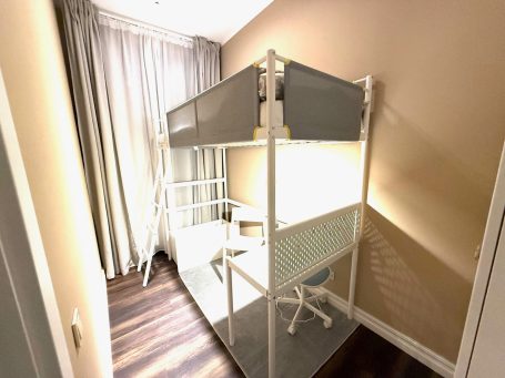 A modern bunk bed with a desk underneath in a cozy, well-lit room.