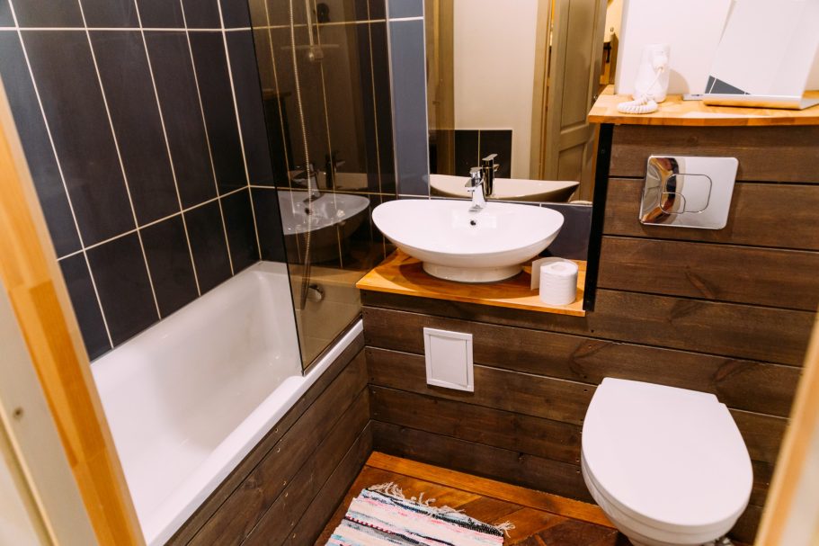 Compact bathroom featuring a bathtub, toilet, sink, and wooden accents.