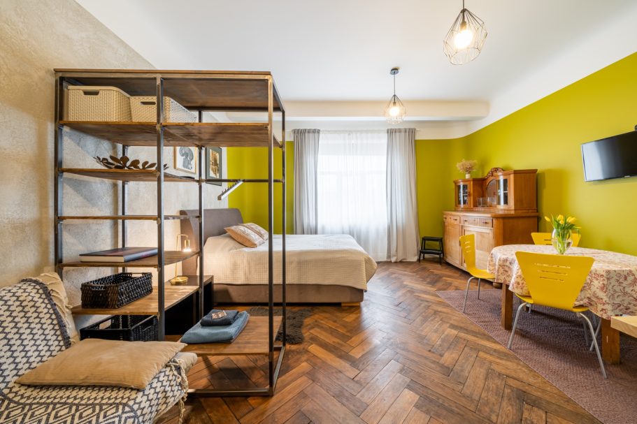 Cozy modern room with green walls, wooden floor, bed, shelving unit, and small dining table.