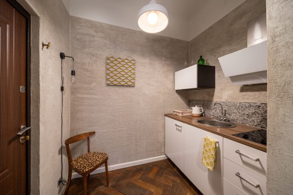 Cozy kitchen with a wood floor, white cabinetry, and a single wooden chair.