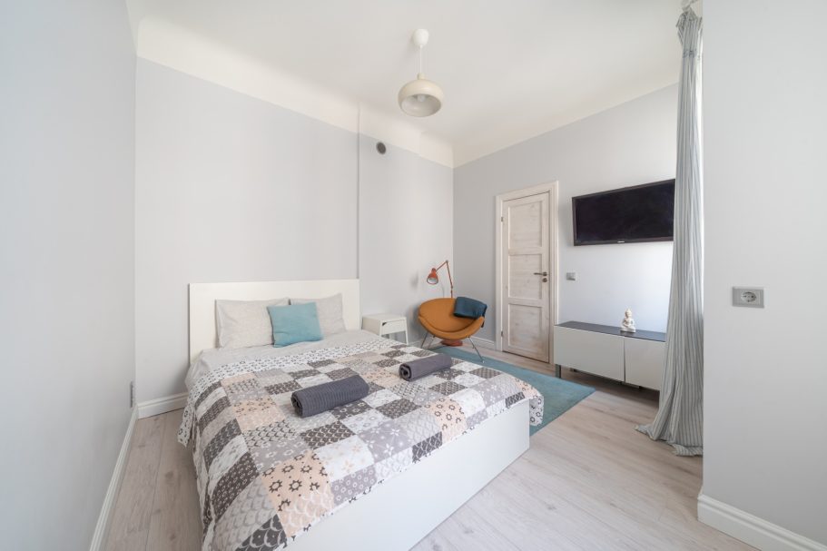Cozy bedroom with a bed, blue accent chair, TV, and light gray walls.