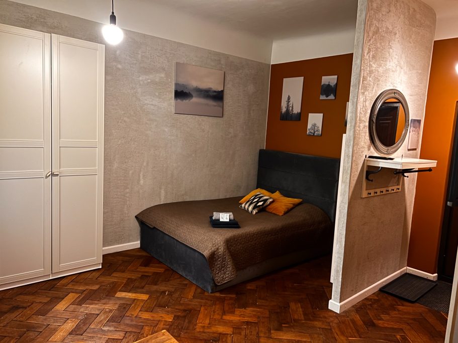 Cozy bedroom with a bed, wardrobe, and warm-colored walls. A mirror and artwork are visible.