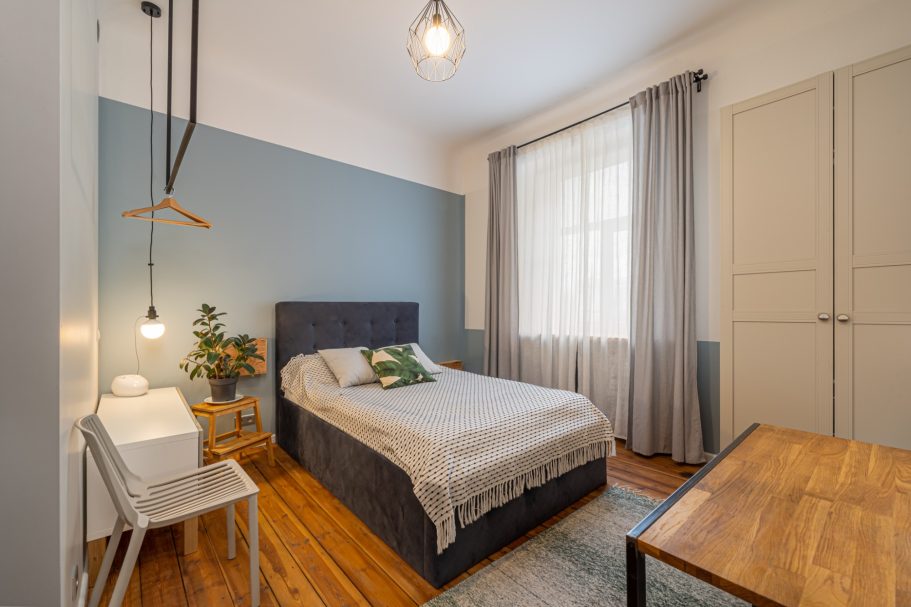 Cozy bedroom featuring a bed, wooden table, and large window with natural light.