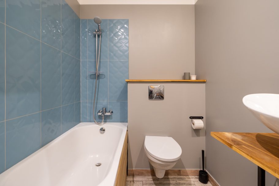 Modern bathroom featuring a bathtub, toilet, and wooden accents against blue tiles.