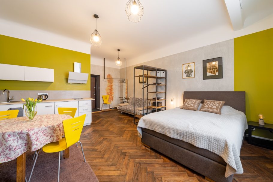 Cozy studio apartment featuring a bed, dining table, and modern kitchen with green accents.