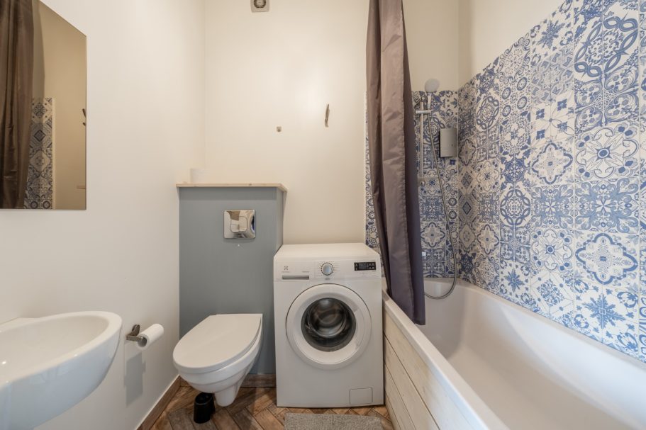 Compact bathroom featuring a bathtub, toilet, washing machine, and decorative tiles.