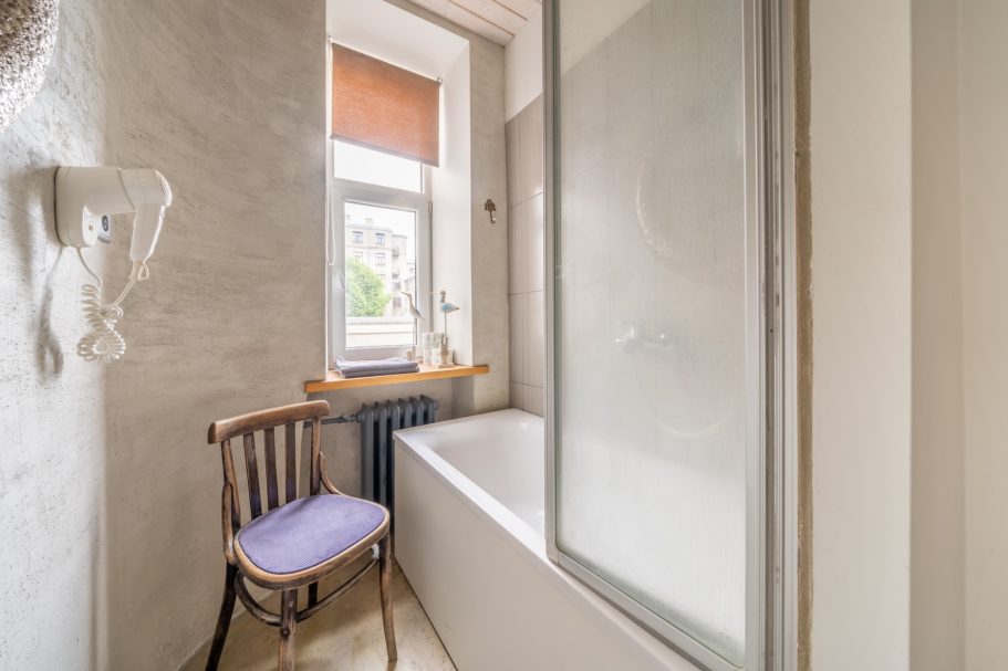 A bathroom with a shower, bathtub, and a wooden chair by the window.