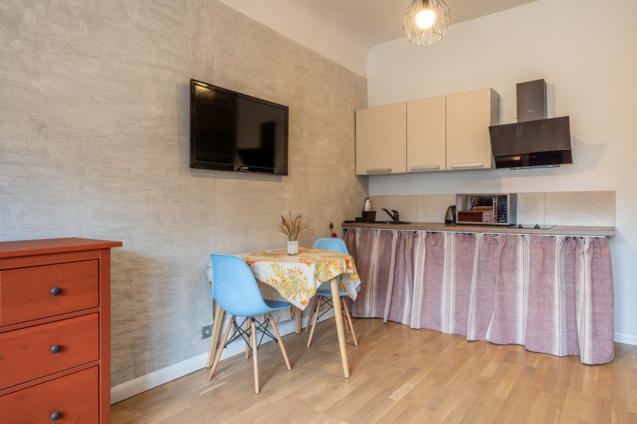 Small kitchen area with a dining table, light cabinets, and a TV on the wall.