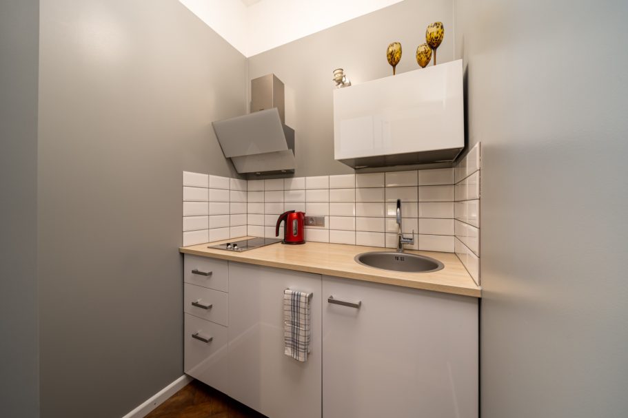 Small kitchen with a sink, countertop, cabinets, and a kettle on the surface.