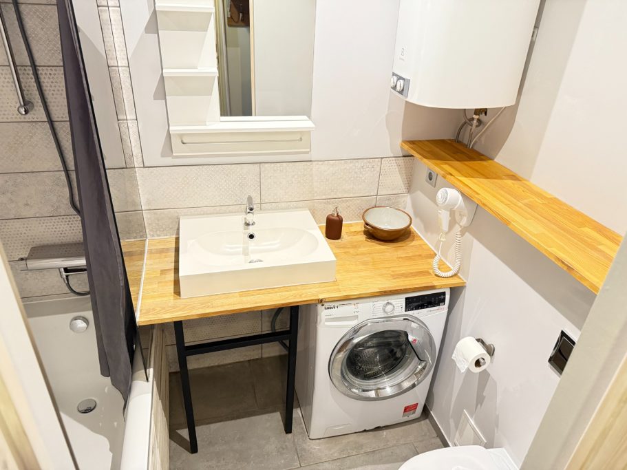 Modern bathroom with a sink on a wooden countertop and a washing machine.