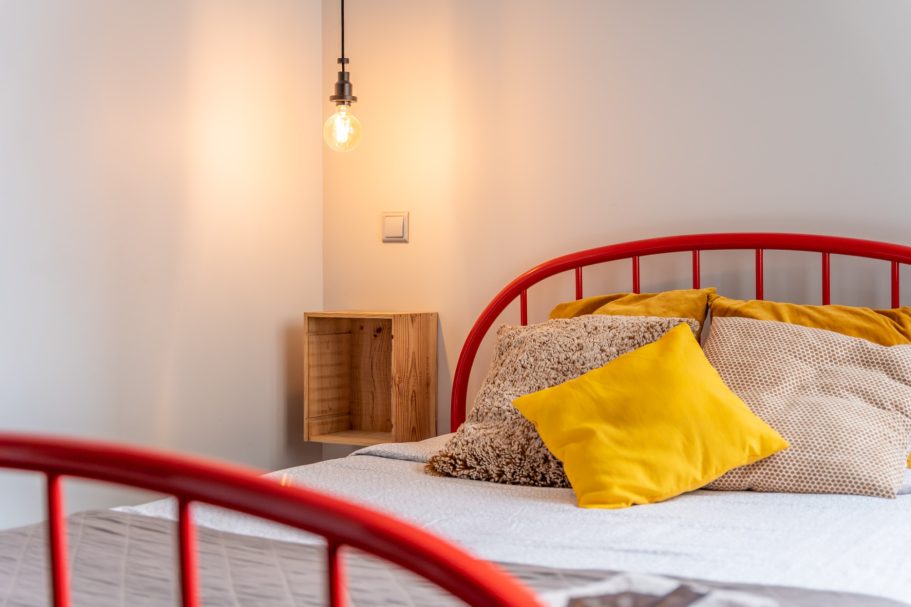 Cozy bedroom with a red metal bed, decorative pillows, and a warm light fixture.