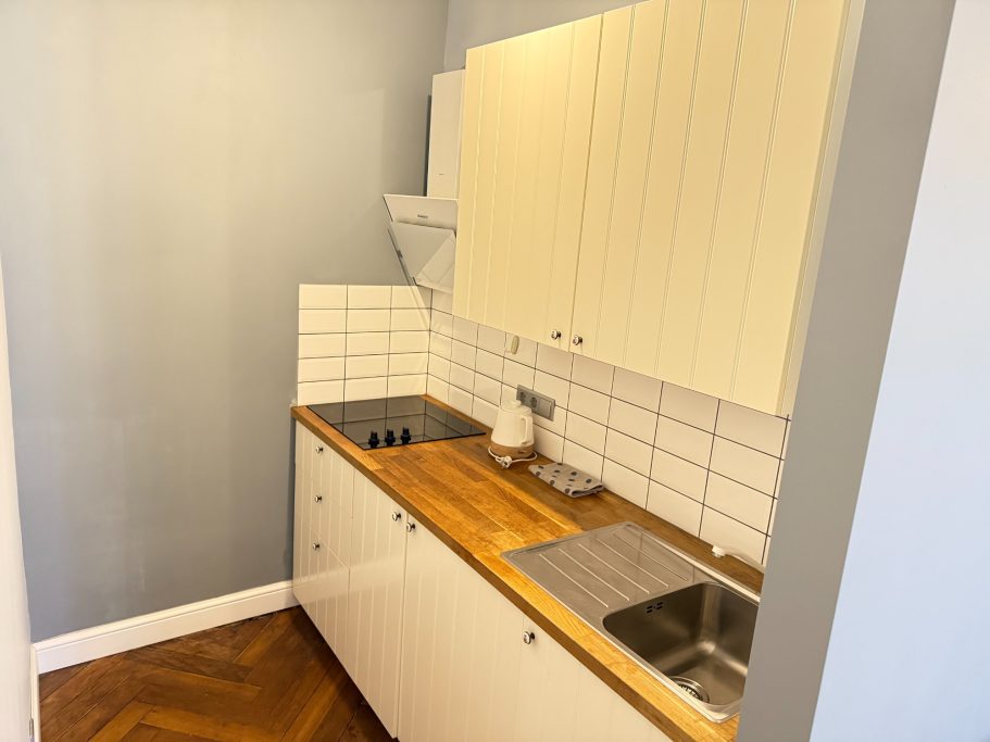 Compact kitchen with wooden countertop, sink, and white cabinets against a light blue wall.