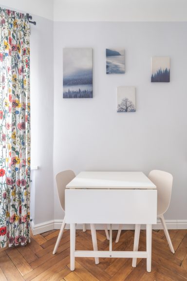 Bright dining area with a white table, two chairs, and colorful floral curtains.